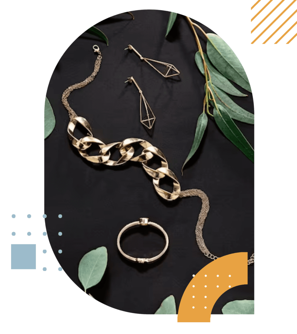 Gold jewelry pieces including a chain, bracelet, and earrings arranged artistically on a dark background with green leaves and abstract shapes.