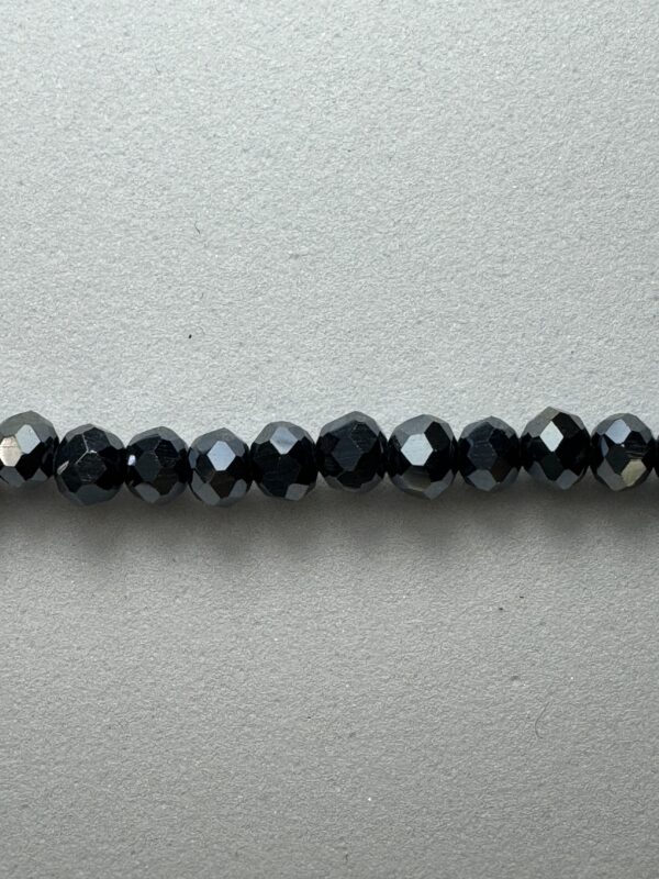 Black faceted beads on grey surface.