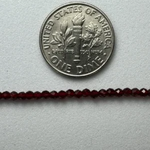 US dime beside red gemstone beads.