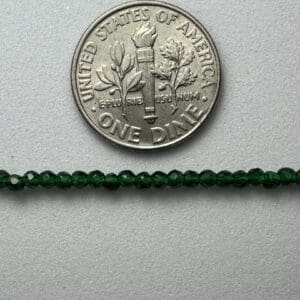 Dark green beads beside a dime.