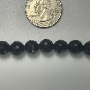 Black faceted beads next to quarter.