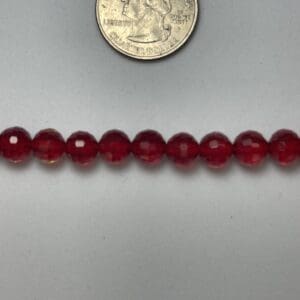 Red glass beads next to quarter.