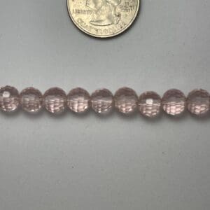 Pink glass beads next to quarter.