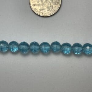 Light blue glass beads next to quarter.