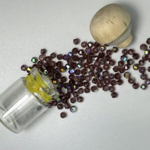 Tipped glass vial spilling iridescent faceted purple beads