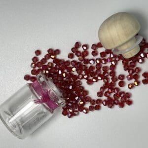 Spilled ruby bicone beads beside glass vial