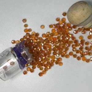 Faceted orange beads scattered from glass vial