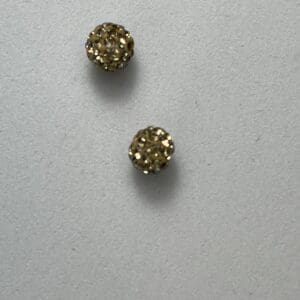 Two gold glittery stud earrings on gray.