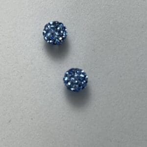 Two blue glittery round earrings on surface.