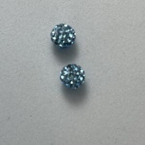 Two blue glittery round earrings on surface.