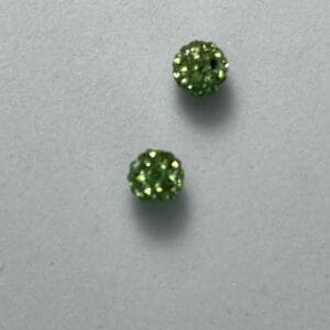 Two sparkly green round earrings on surface.