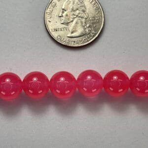 Pink gemstone beads with quarter for scale.