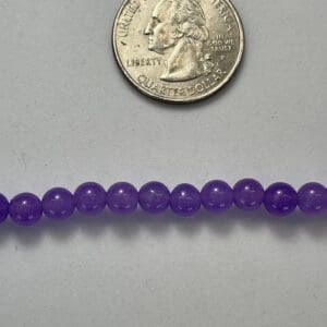 Purple beads next to a quarter.