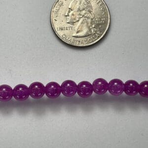 Purple beads next to a quarter.